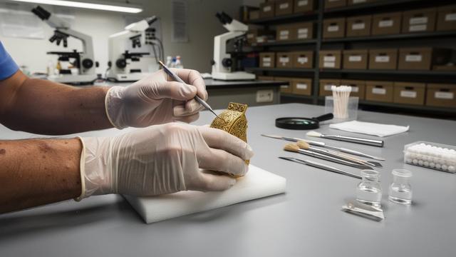 خبير ترميم يعمل بأدوات دقيقة أمام قطعة ذهبية
